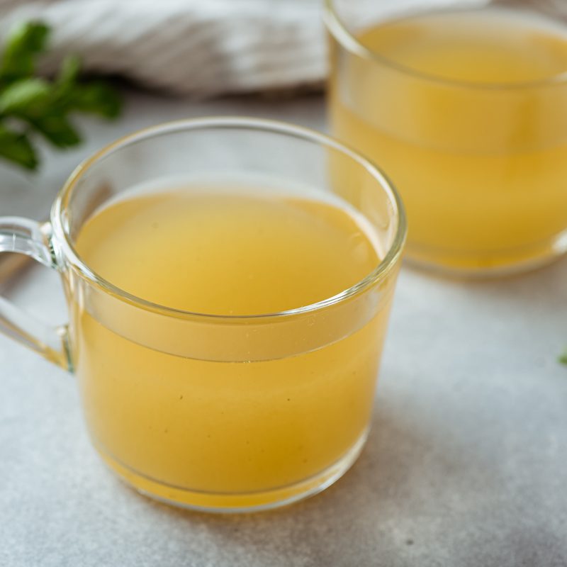 Bone broth in a glass cup on a light background, selective focus