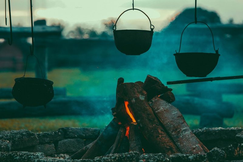 A smoldering campfire heating up an iron pot in the dusk