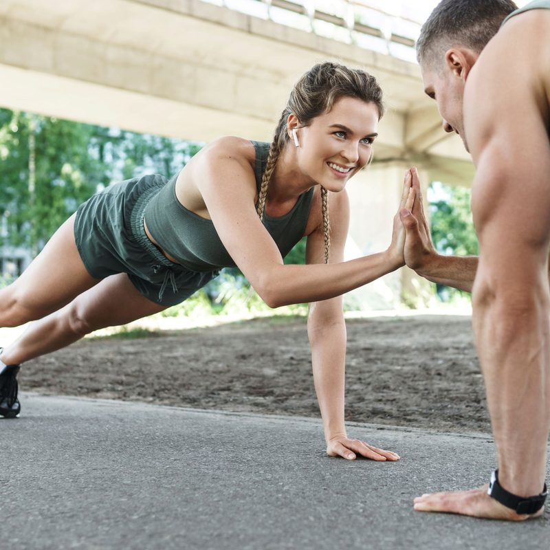 Man and woman working out plank pose joining hands outside on concrete
