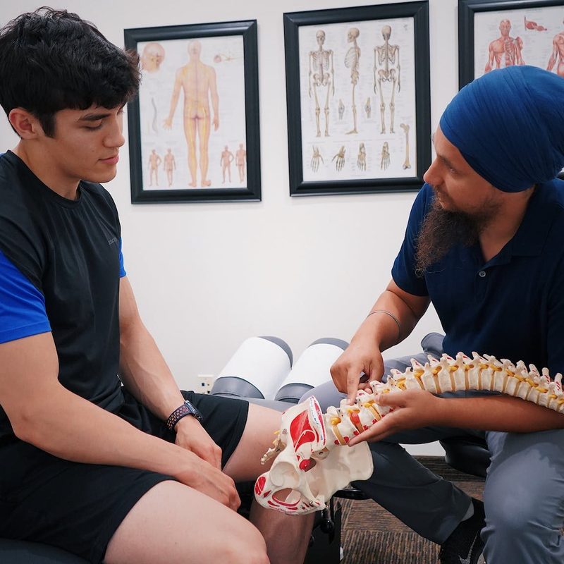 Doctor or healthcare professional discussing bone health and showing model of spine to patient sitting on bed in office