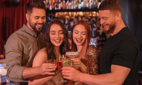 Happy friends clinking glasses with fresh cocktails in bar