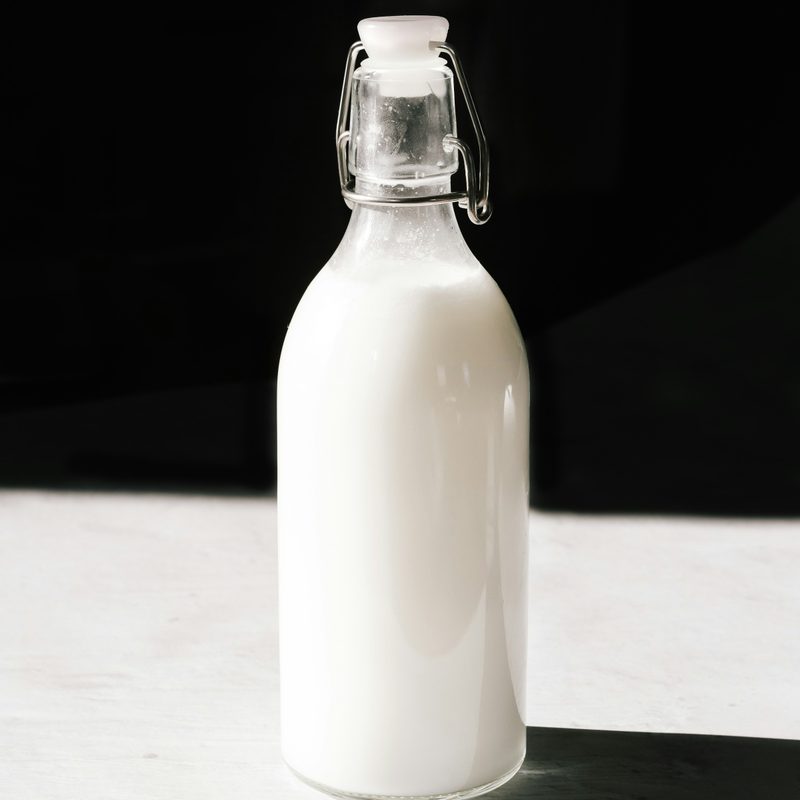 Glass bottle of milk on white table with black background