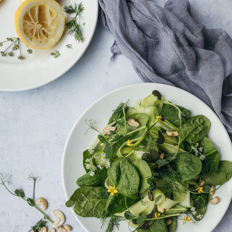Leafy greens salad on white plate with sliced lemons on white table