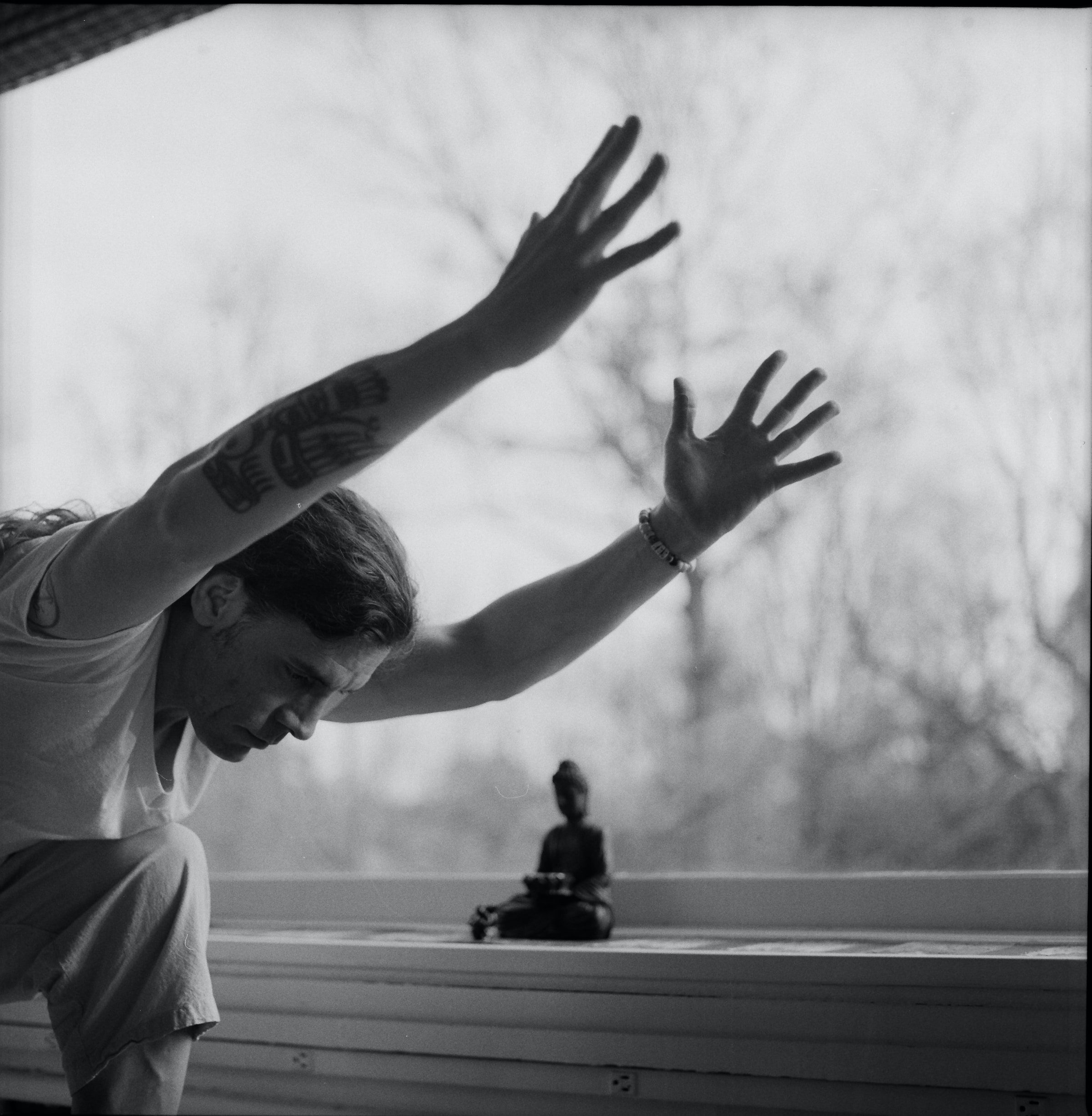 man doing yoga in front of Buddha statue raising arms black and white image