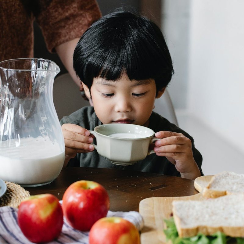 Little boy drinking milk and sitting at table wth apples and lots of food