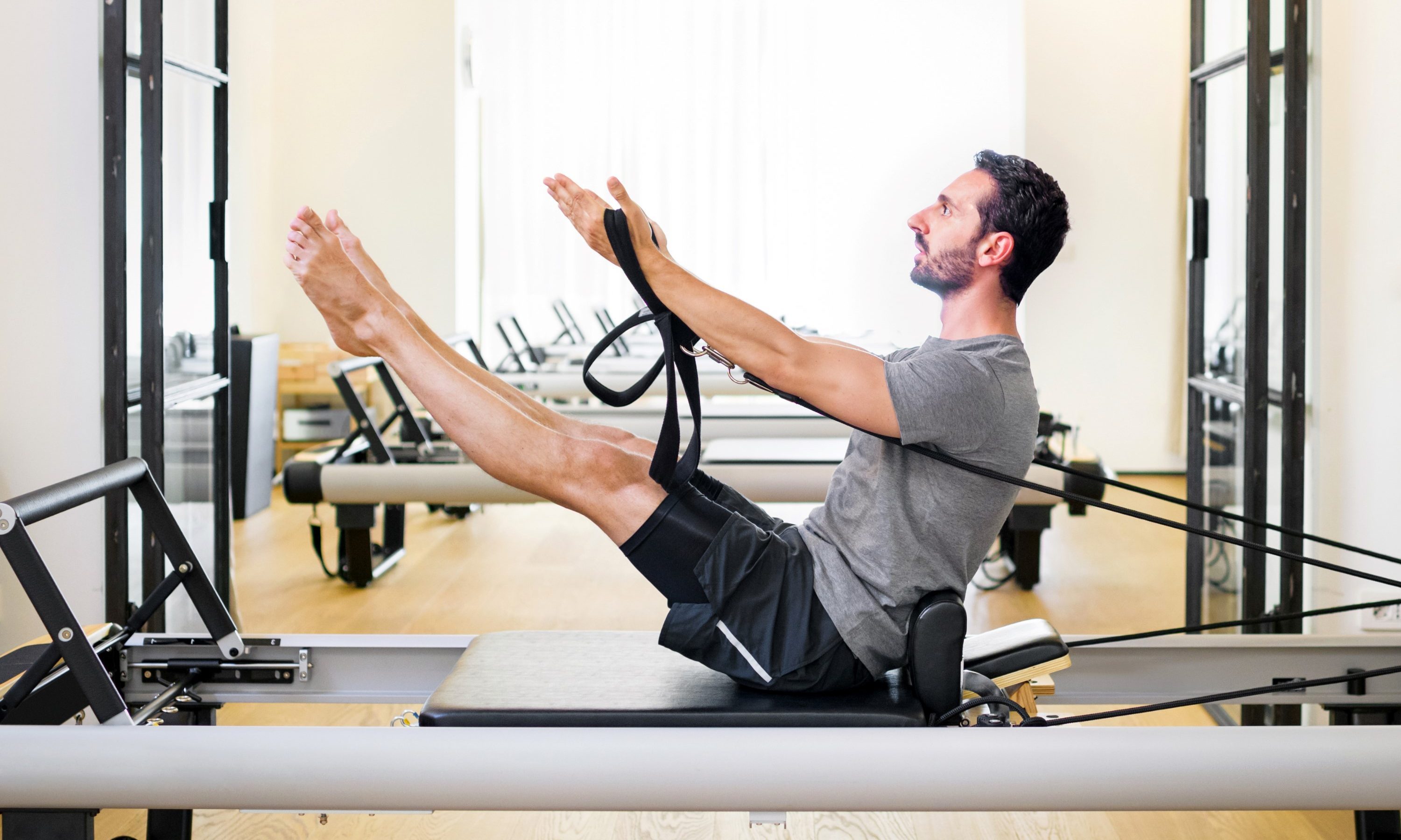 man doing pilates leg and arm stretch seated wooden floor