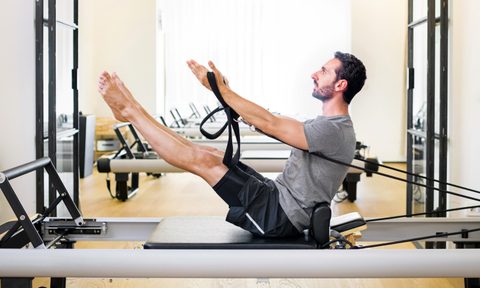 Man doing Pilates leg and arm stretch seated wooden floor