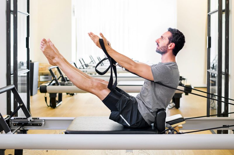 man doing pilates leg and arm stretch seated wooden floor