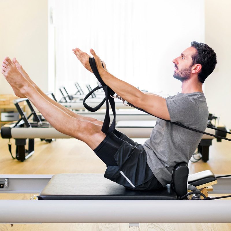 Man doing Pilates leg and arm stretch seated wooden floor