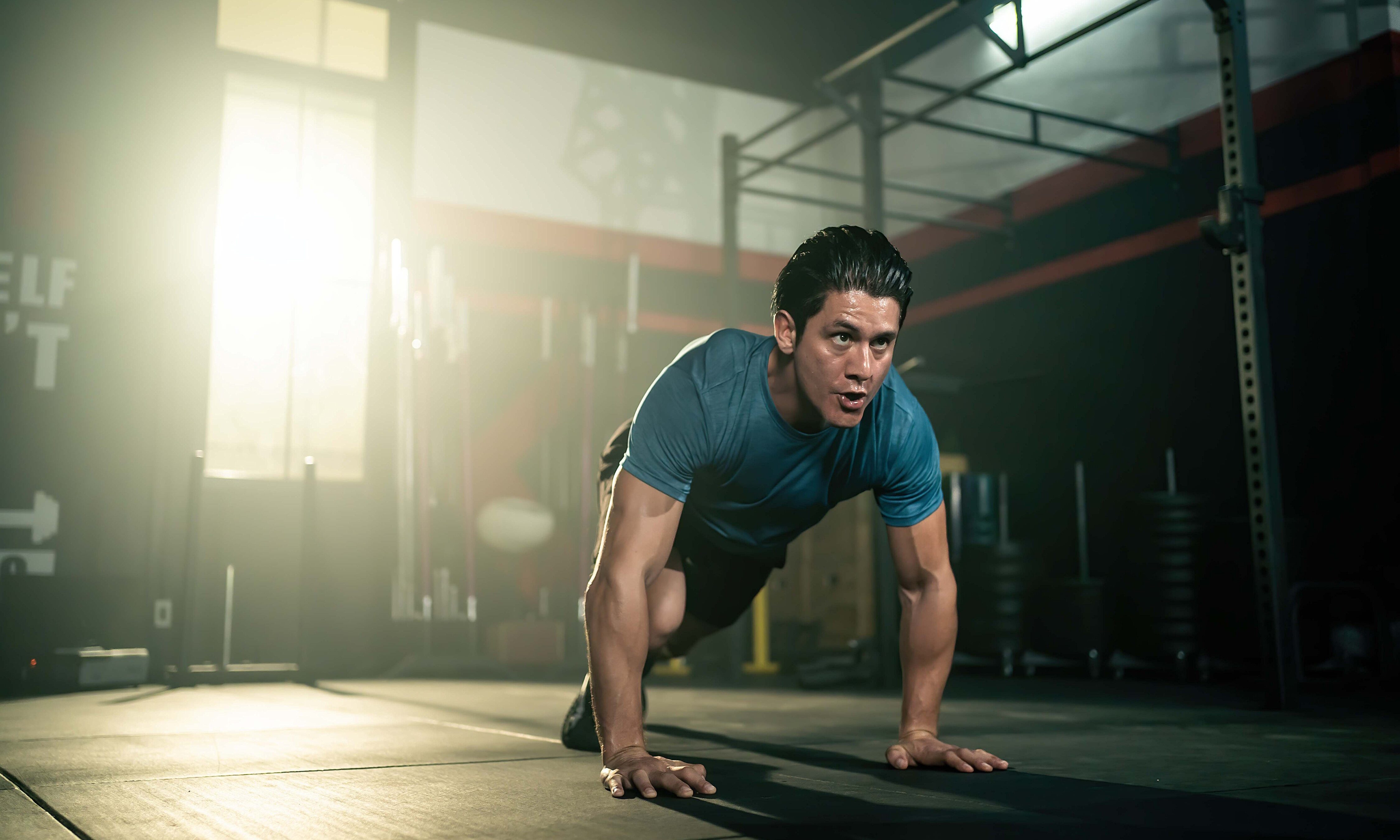 man doing pilates on mat on floor running pose wearing blue shirt