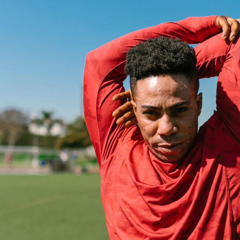 A man in a red shirt doing an overhead triceps stretch