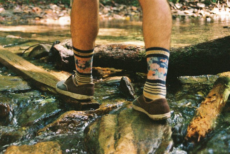 man walking on river rocks with high socks