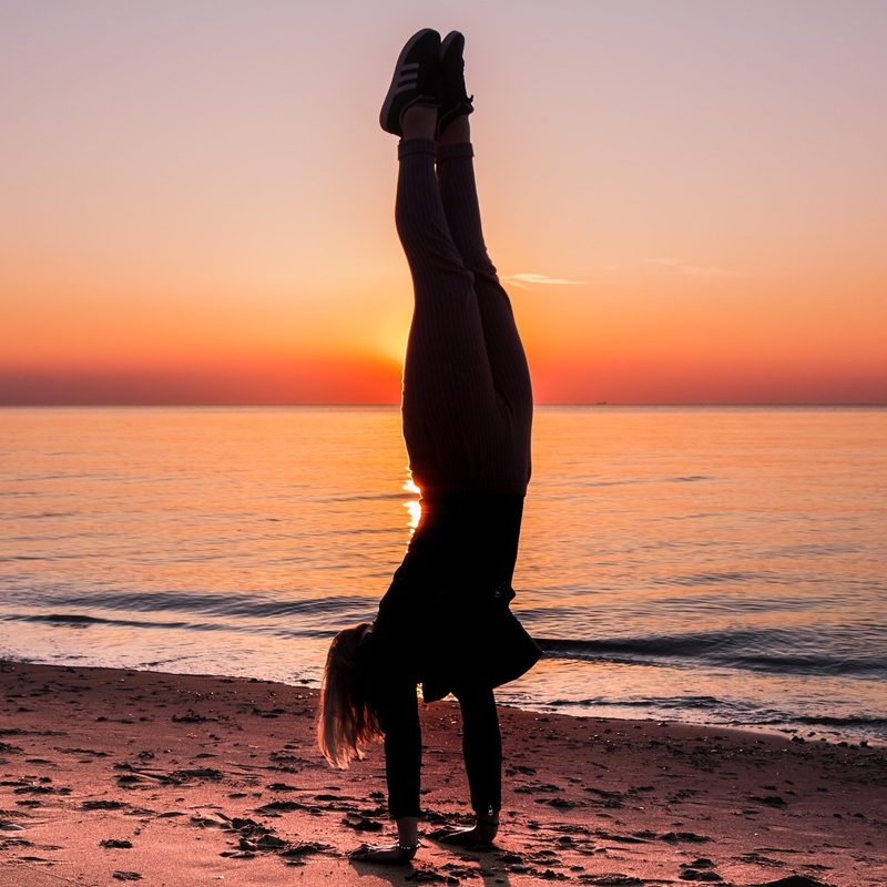 Silhouette of a woman doing handstand by the ocean water on the beach at sunset