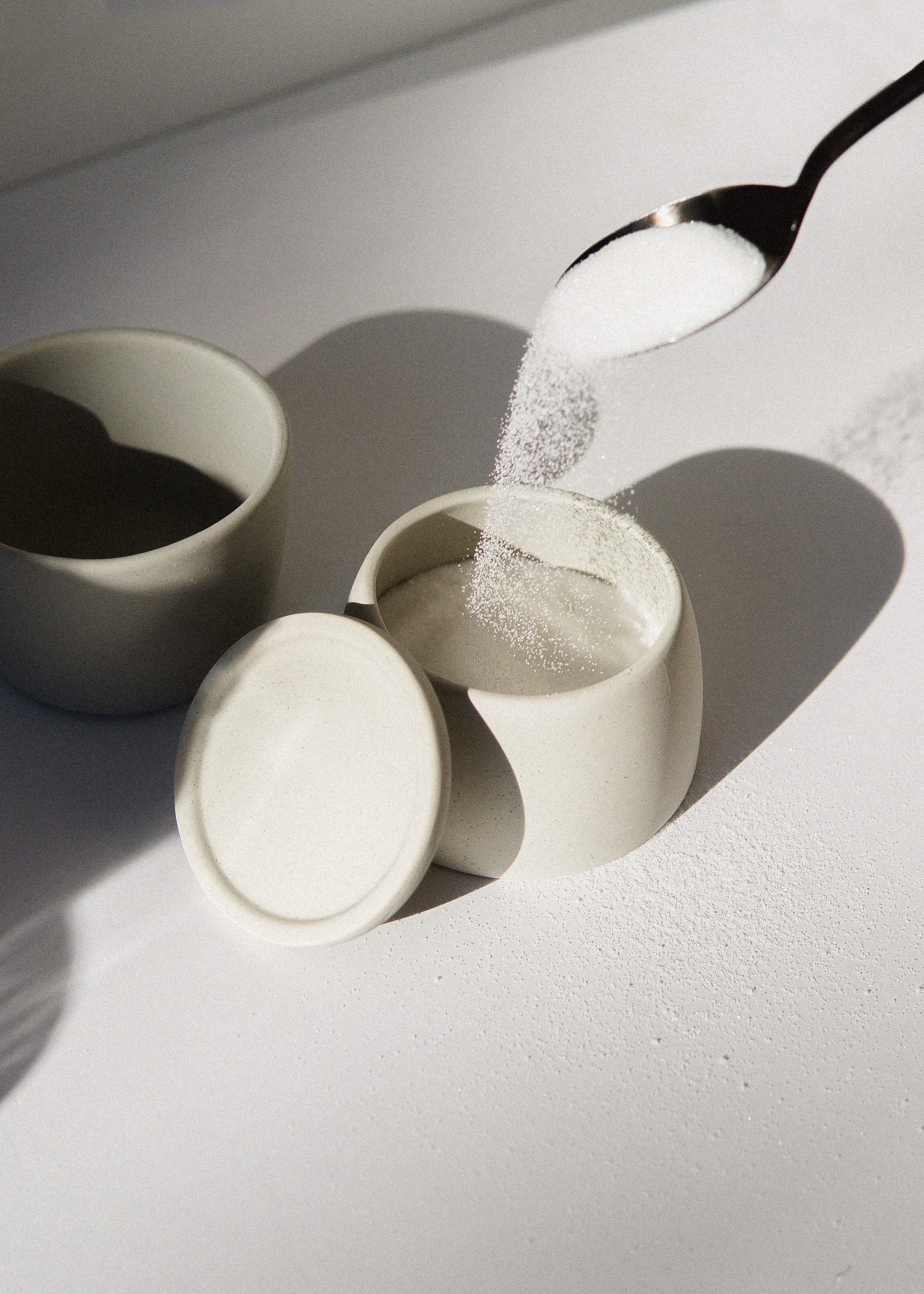 white sugar pouring from silver spoon into white ceramic container with white background