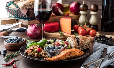 Mediterranean meal of greek salad, seven grain salad, salmon fillet and a small bowl of blueberries, surrounded by Mediterranean diet foods.