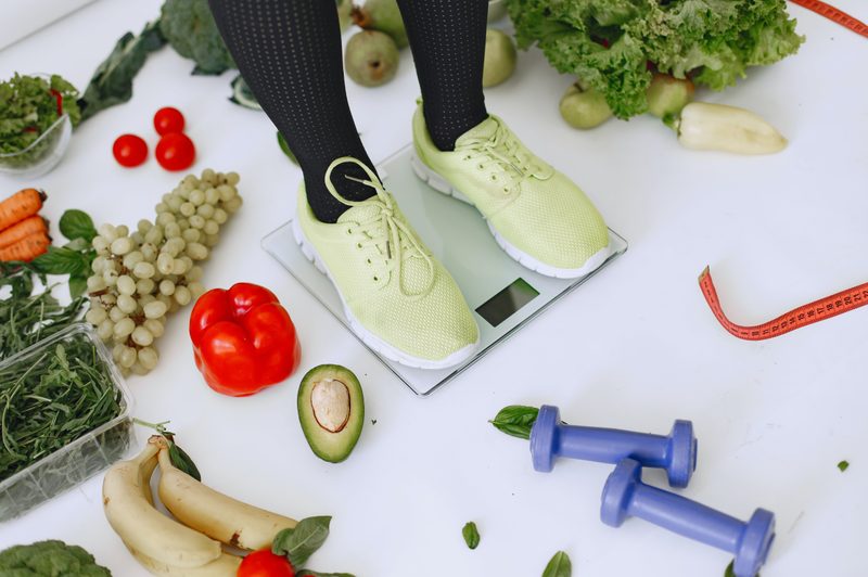 Person standing on scale with weights and healthy food surrounding the scale