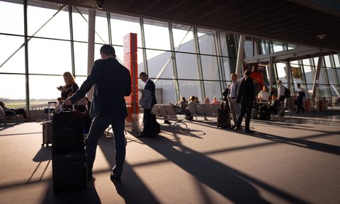 Interior of an airport with people stanidng in the shadows in front of a window
