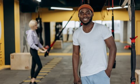 Man smiling to the camera with woman working out behind him