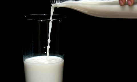 Pouring milk from a glass bottle into a glass with a black background