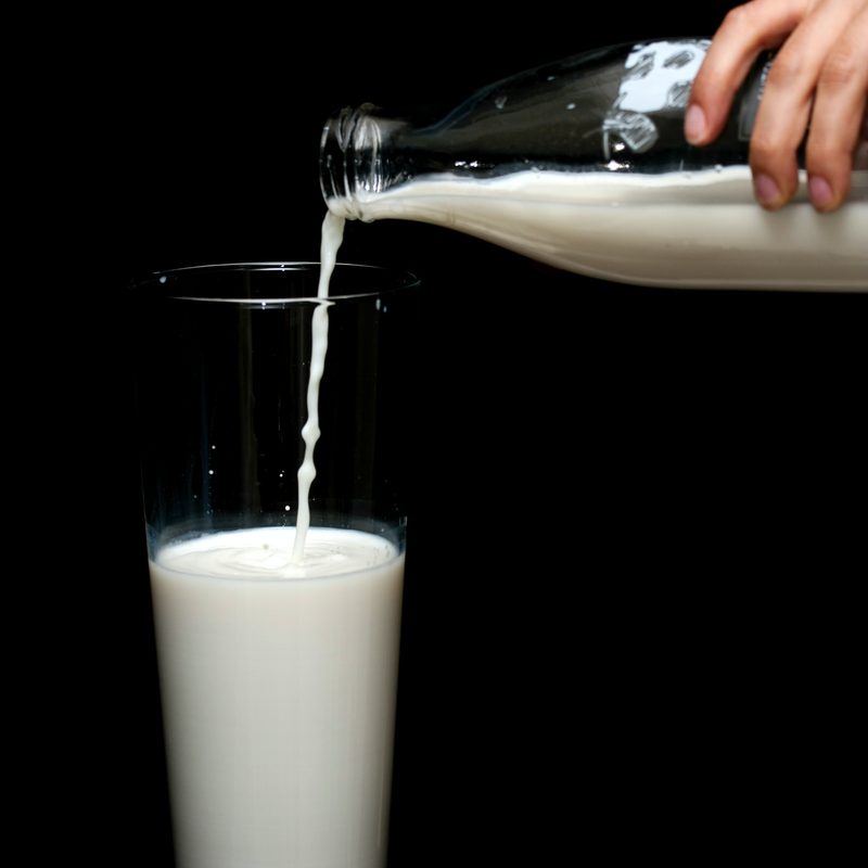 Pouring milk from a glass bottle into a glass with a black background