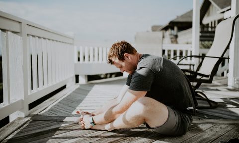 man sitting cross legged in a yoga pose on a porch outside by a white fence