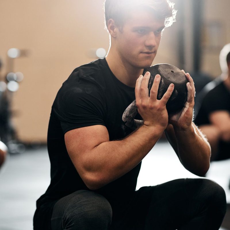 Young males doing squats with weights at the gym