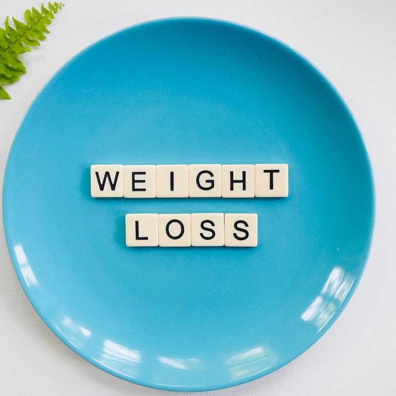 Blue plate with word blocks text weight loss on white background with green leaf