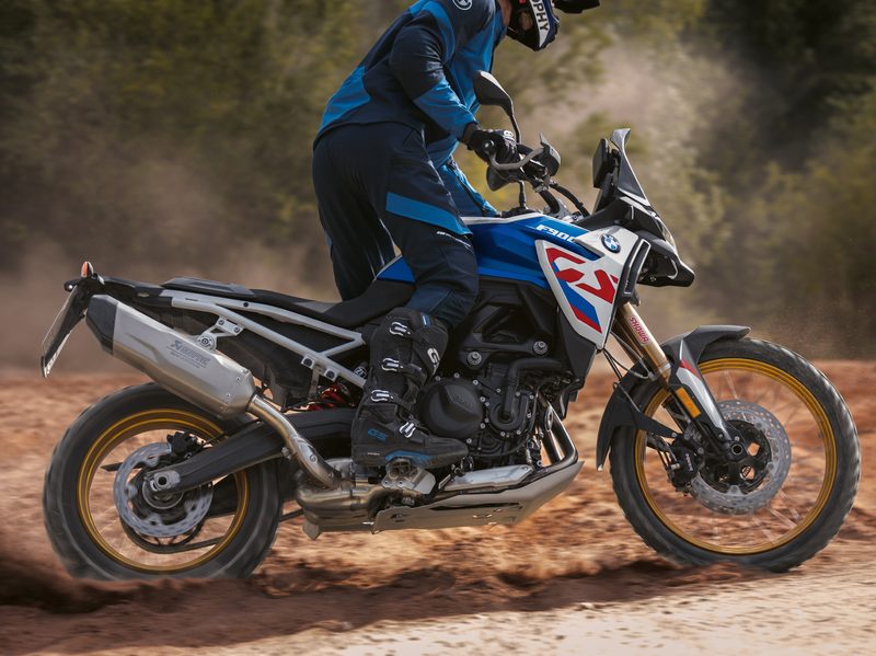A rider standing on pegs riding a 2024 BMW F 900 GS in dirt.