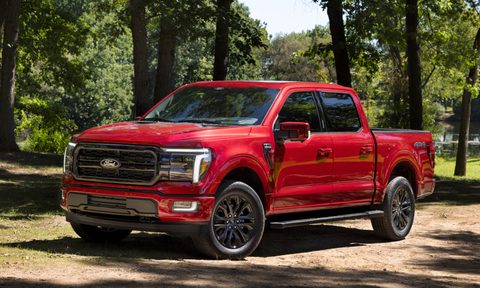 2024 Ford F-150 Lariat pickup truck front left three-quarter view parked on grass in front of trees.
