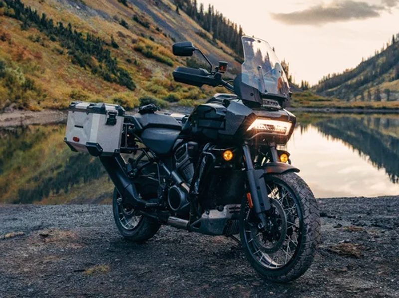 2024 Harley-Davidson Pan America 1250 Special motorcycle parked by a pond with sloping hills in the background.