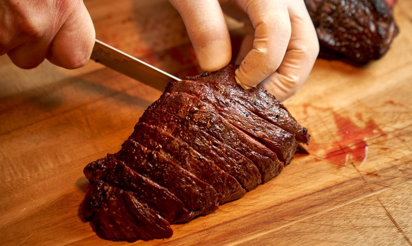 Hand slicing picanha steak on cutting board.