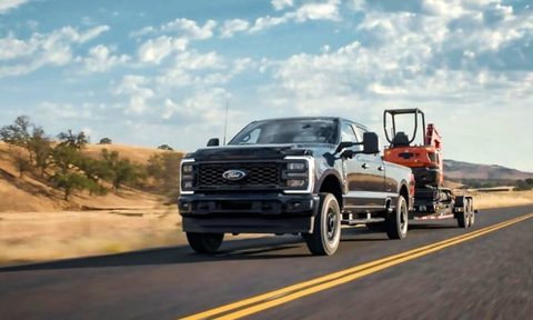 Ford F Series SuperDuty pickup truck towing a trailer carrying a piece of construction equipment on a highway.