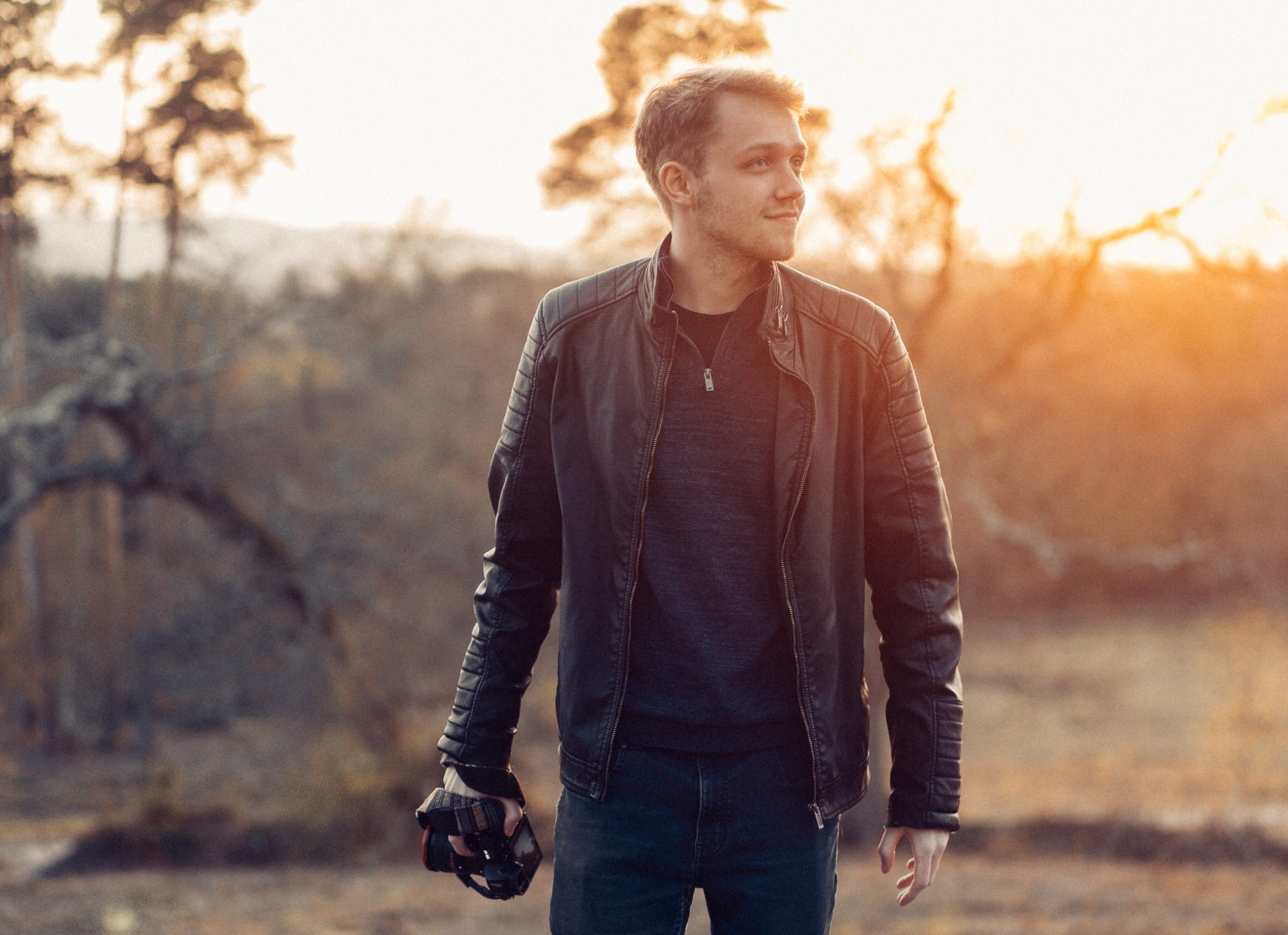 Man in leather jacket in woods with camera