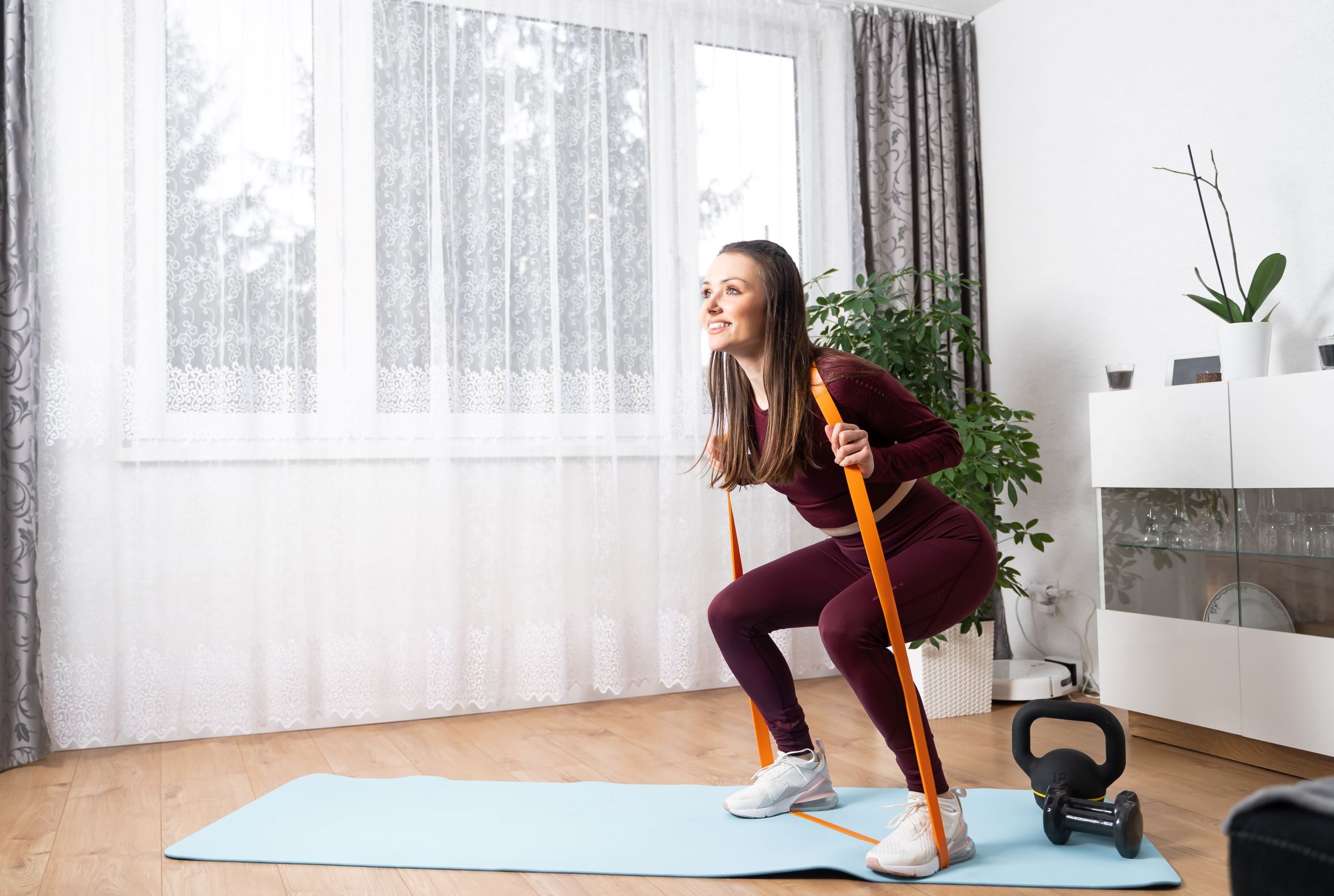 woman doing a squat exercise holding a resistance band indoors