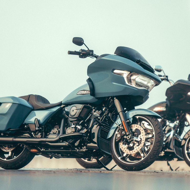 Two 2024 Harley Davidson Road Glides parked on concrete with a person standing on the right margin of the frame.