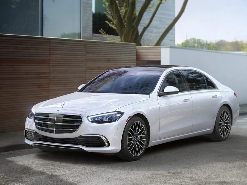 White 2024 Mercedes-Benz S 580e hybrid parked on a city street next to a sidewalk.