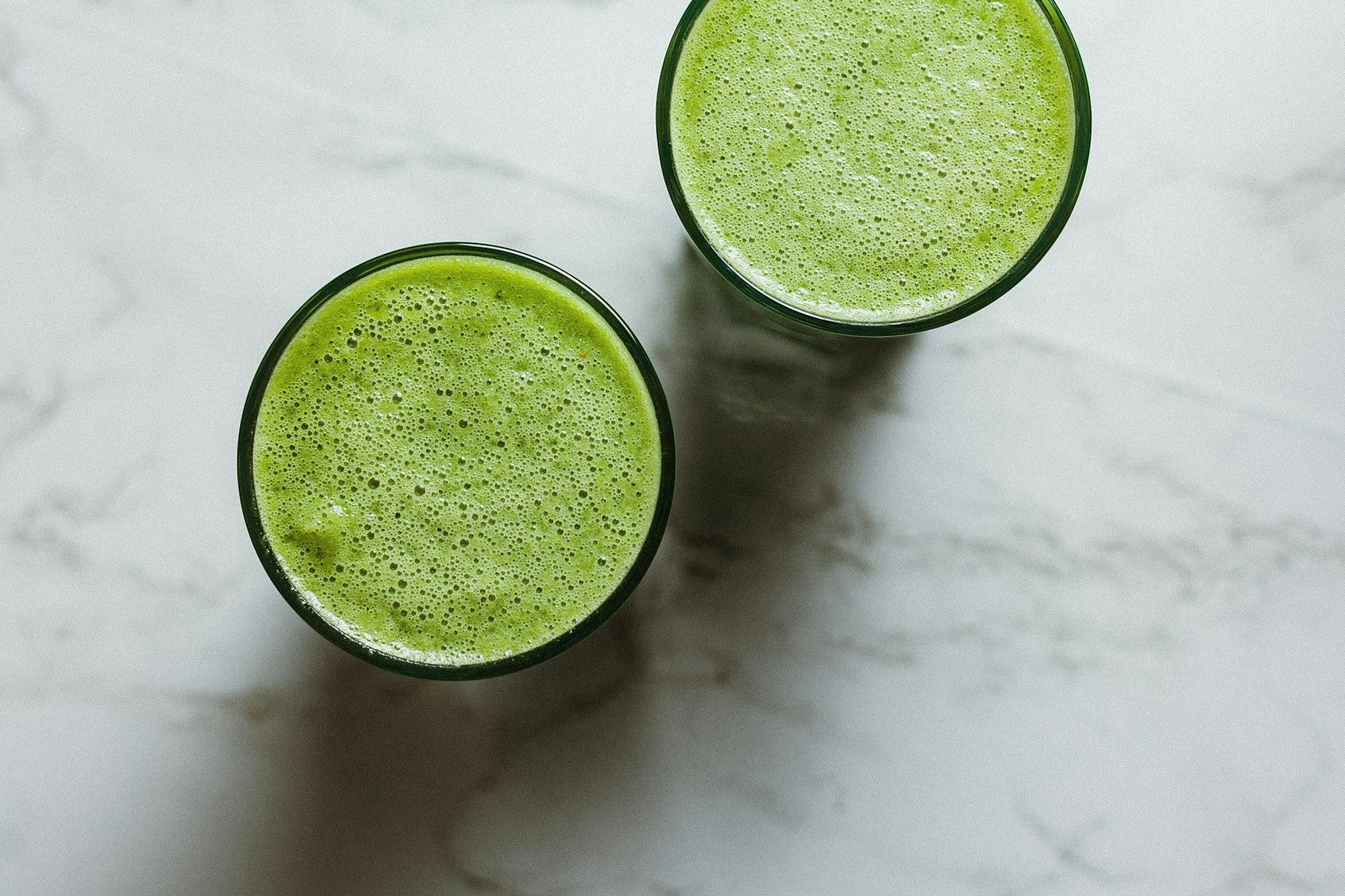birds eye view of two glasses of green drink or celery juice on white stone table
