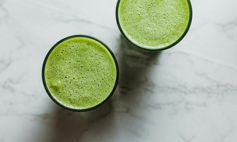Bird's-eye view of two celery juice drinks on white stone table
