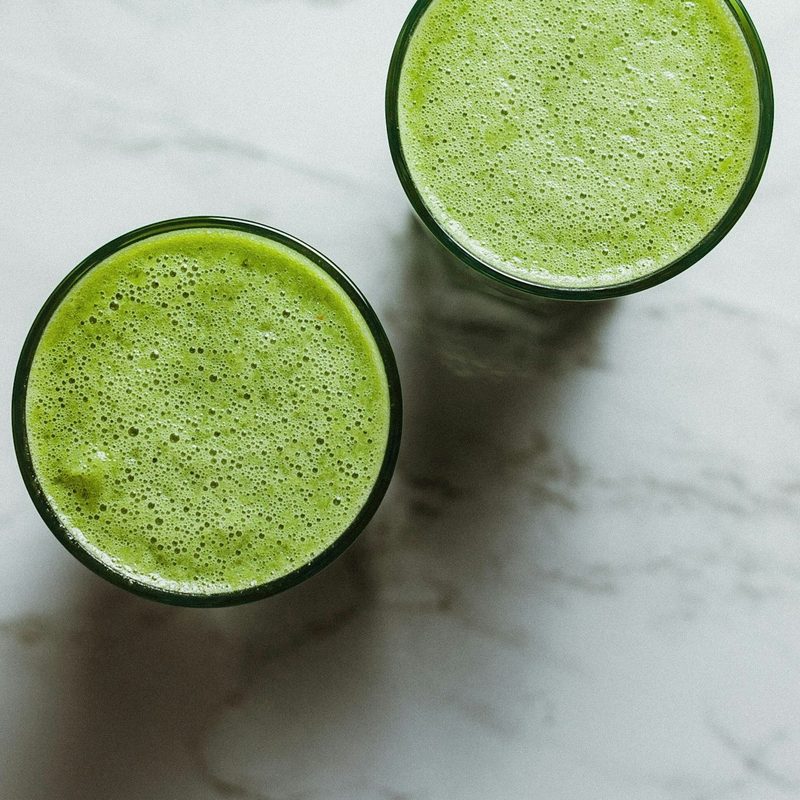 Bird's-eye view of two celery juice drinks on white stone table