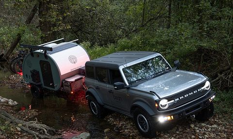 A Bean Stock 2.0 ultralight travel trailer being towed down a wooded trail by a new Ford Bronco.