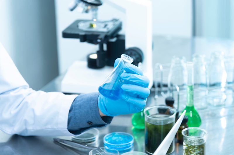 Close up of a hand with glove on holding a test tube full of blue liquid