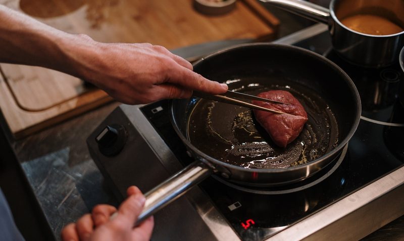 Person cooking a steak in a pan