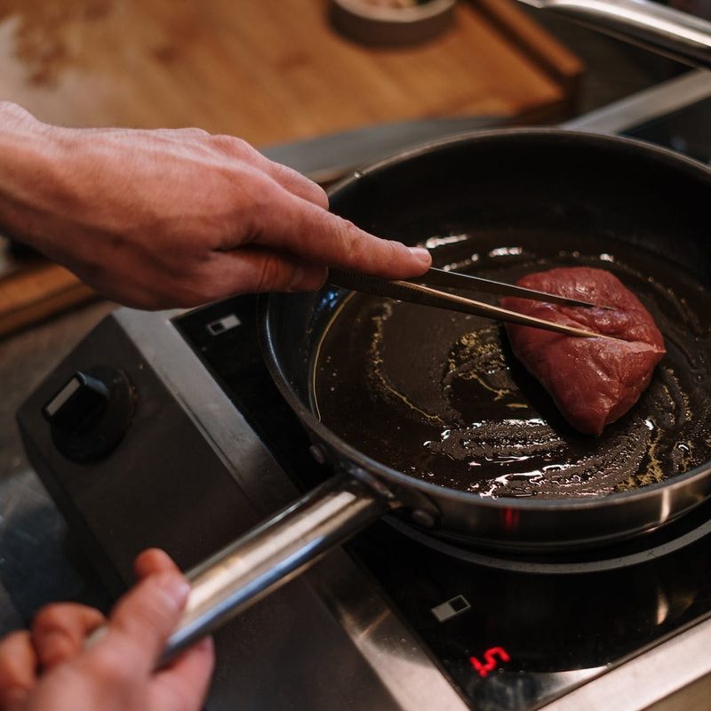 Person cooking a steak in a pan