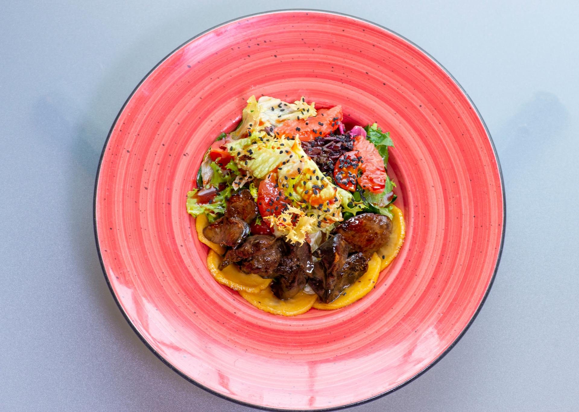 liver and vegetable salad dish on red plate with a light blue background