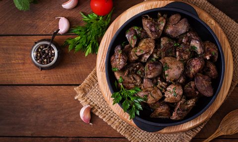 liver and onion on skillet on wood on table next to onions and herbs