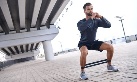 Young sportive man uses resistance band for exercising outdoors