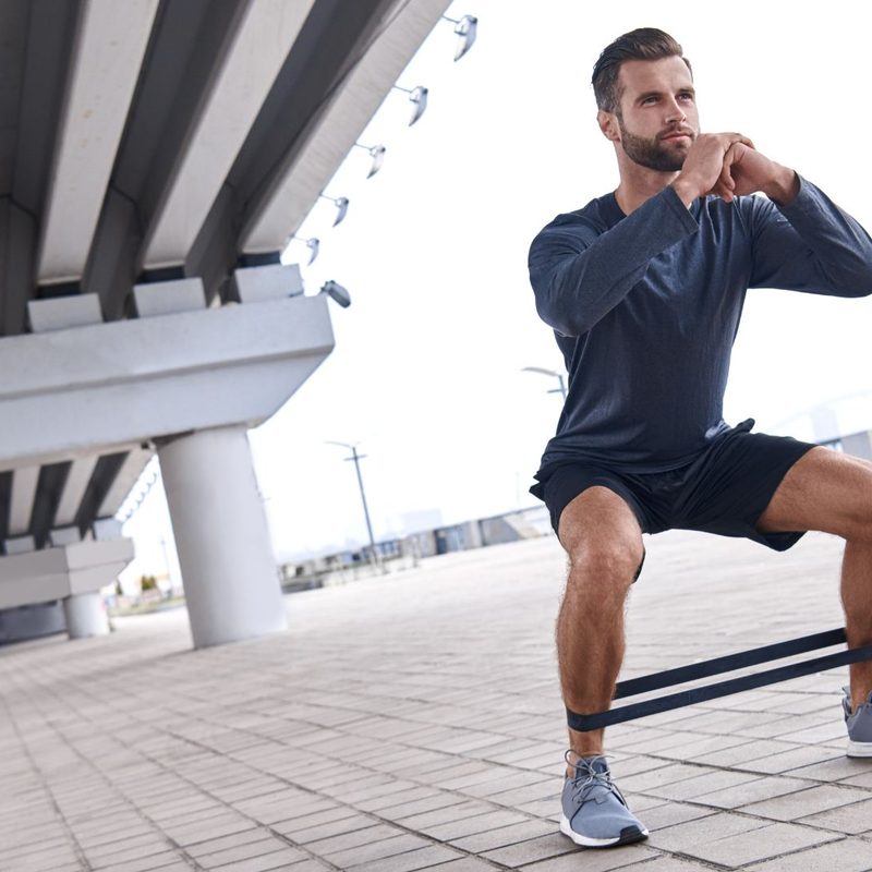 Young sportive man uses resistance band for exercising outdoors