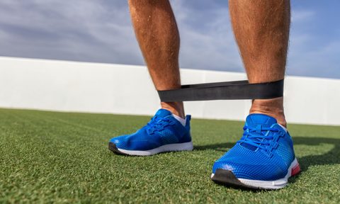 Man wearing resistance band on his ankle in blue tennis shoes