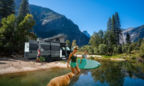 Young couple stepping into mountain stream with Westfalia Wave van in the background.
