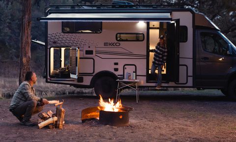 Man building a campfire in front of a Winnebago Ekko Springer camper van.